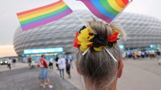 Symbolbild: Eine Frau mit LGBTQ-Fähnchen im Haar steht vor der EM-Arena in München. (Quelle: dpa/C. Charisius)