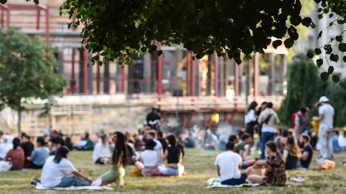 Mehrere Personengruppen sitzen am Abend bei warmen Wetter im James-Simon-Park. (Quelle: dpa/Kira Hofmann)