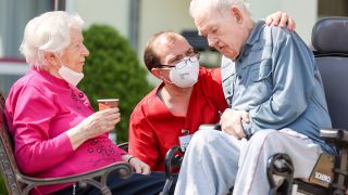 Symbolbild: Ein Altenpfleger spricht auf dem Hof eines Seniorenheims mit älteren Heimbewohnern. (Quelle: dpa/J. Woitas)