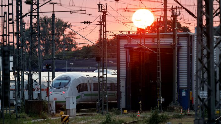 Symbolbild: Mehrere Züge stehen bei Sonnenuntergang neben einer Wartungshalle