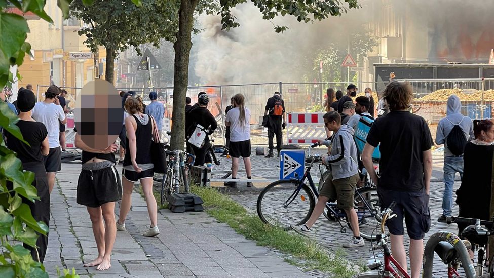 Menschen stehen vor einer Straßenabsperrung und brennenden Barrikaden auf der Rigaer Straße in Berlin Friedrichshain. (Quelle: rbb)