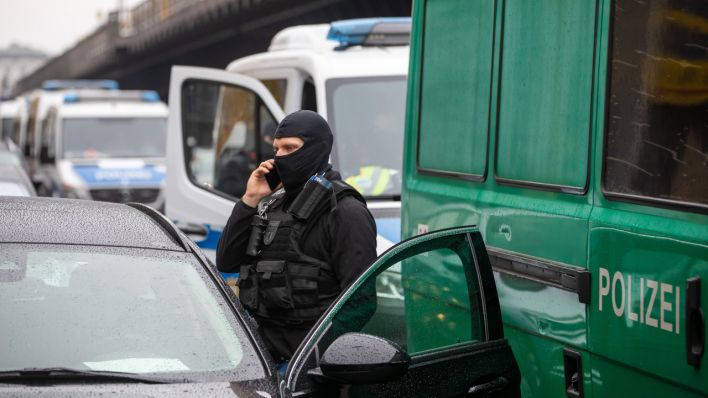 Ein Polizist telefoniert bei einer Razzia in Berlin (Quelle: dpa/Christoph Soeder)