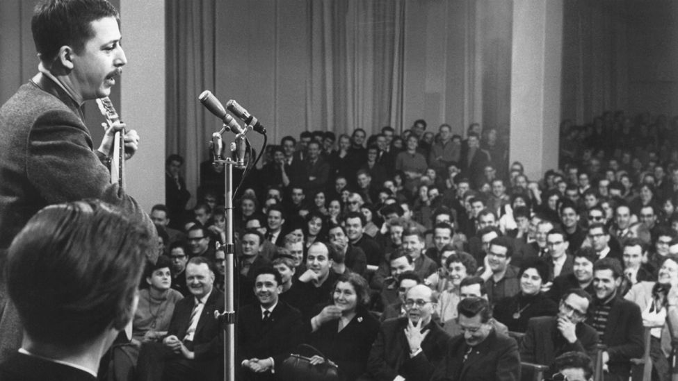 Der Liedermacher Wolf Biermann (l.) trägt am 08.01.1963 im überfüllten Marx-Engels-Auditorium der Ostberliner Humboldt-Universität zum VI. Parteitag der SED zwei Balladen mit Gitarrenbegleitung vor. (Quelle: dpa/ADN)