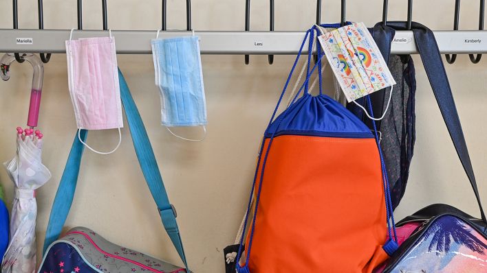 Masken hängen im Mai 2021 zusammen mit Taschen und Rucksäcken an Kleiderhaken in einem Klassenraum einer Grundschule. (Quelle: dpa/Patrick Pleul)
