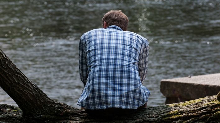 Ein Mann sitzt am 17.07.2013 in Berlin allein auf einem Baumstamm am Landwehrkanal. (Quelle: dpa/Paul Zinken)