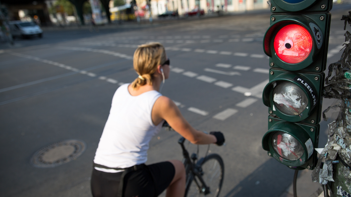 Archivbild: Eine Radfahrerin fährt am 12.08.2015 in Berlin über die Strasse, wahrend im Vordergrund eine Radfahrerampel rot zeigt. (Quelle: dpa/Florian Schuh)