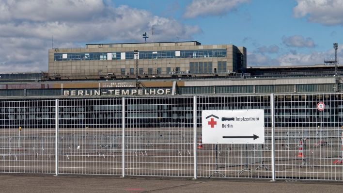 Blick auf das Flughafengebäude Tempelhof im Vordergrund steht auf einem Schild "Corona Impfzentrum Berlin" (Quelle: Picture Alliance/Global Travel Images)