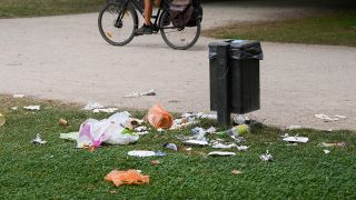 Ein Mülleimer und danebenliegender Müll im Treptower Park. (Quelle: dpa/Jens Kalaene)