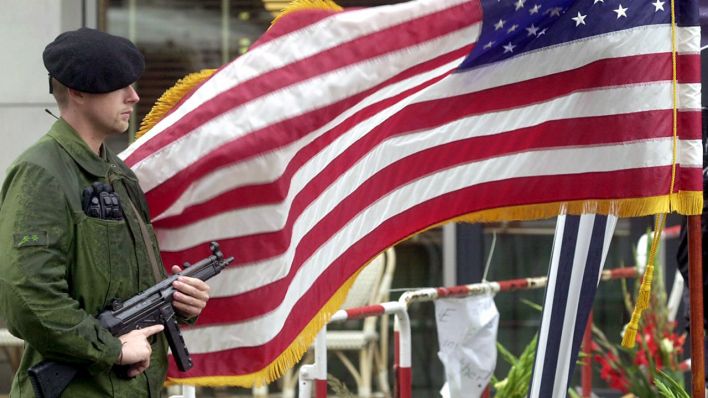 Ein Polizist mit einer Maschinenpistole in der Hand steht am 13.9.2001 neben einer wehenden Nationalflagge der USA an der amerikanischen Botschaft in Berlin. (Quelle: dpa/Peter Endig)