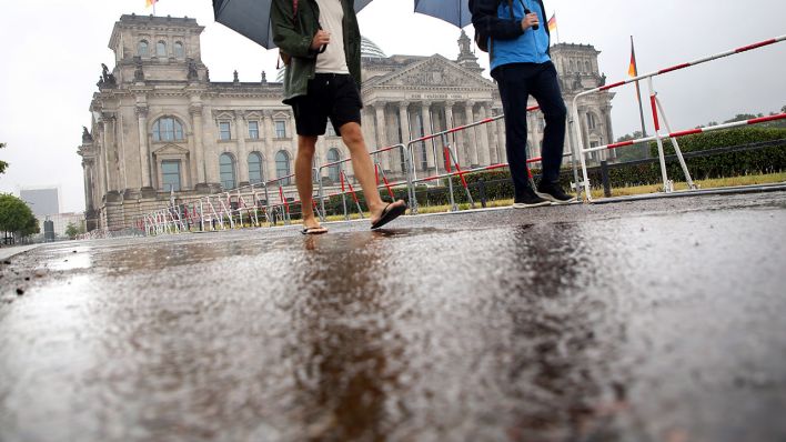 An großen Pfützen, die sich nach Starkregen vor dem Reichstagsgebäude gebildet haben, laufen Touristen bei anhaltendem Regen vorbei. (Quelle: dpa/Wolfgang Kumm)