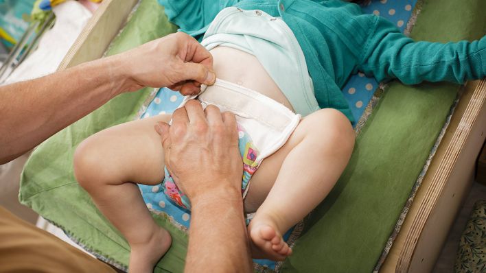 Ein Kleinkind bekommt eine Stoffwindel angezogen. (Quelle: imago images/Thomas Trutschel)
