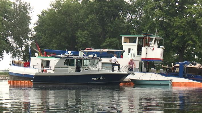 Ein Polizeiboot liegt auf dem Sacrow-Paratzer Kanal bei Potsdam neben einem havarierten Güterschiff, das beim Beladen gebrochen und teilweise gesunken ist. (rbb)