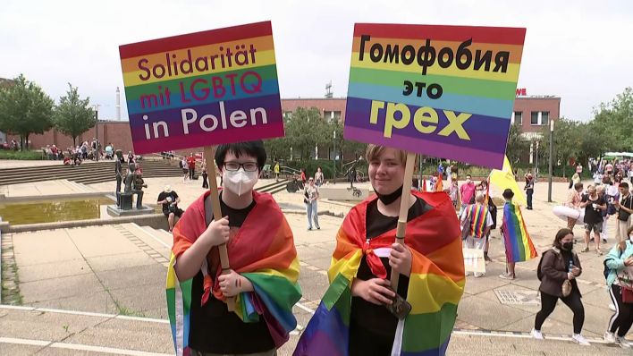 Zwei Teilnehmerinnen des zweiten "Marzahn Pride" halten Protestschilder in den Händen und haben Regenbogenfahnen umgebunden. (Quelle: rbb/Abendschau)