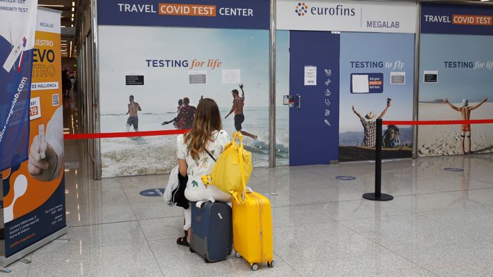 Eine Frau sitzt am 01.08.2021 vor dem Testzentrum am Flughafen von Palma de Mallorca auf Koffern. (Quelle: dpa/Clara Marais)