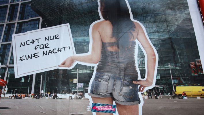 Eine junge Frau in kurzen Hosen hält auf einem Werbeplakat ein Schild mit der Aufschrift "Nicht nur für eine Nacht". Feministinnen haben einen Aufkleber mit den Worten "Sexistische Kackscheisse", auf den linken Oberschenkel der Frau auf dem Plakat geklebt. (Quelle: Wolfram Steinberg/dpa)