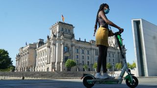 Eine Frau mit Mundschutz fährt auf einem E-Scooter am Reichstagsgebäude vorbei (Quelle: DPA/Jörg Carstensen)