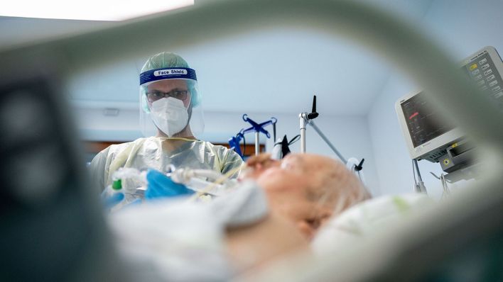 Ein Intensivpfleger steht in Schutzausrüstung an einem Krankenbett (Quelle: DPA/Kay Nietfeld)