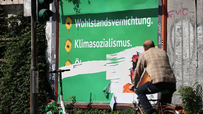 Ein beschädigtes Plakat mit den Schriftzügen "Wohlstandsvernichtung" und "Klimasozialismus" hängt am Straßenrand (Bild: dpa/Oliver Berg)
