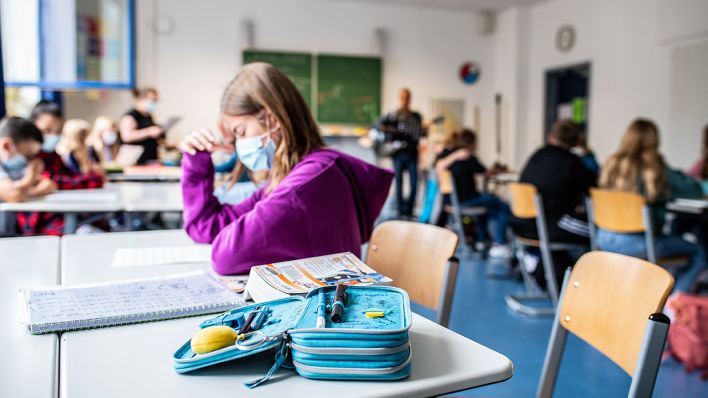 Eine Schülerin sitzt mit ihrer Maske neben ihrem Etui, das auf ihrem Tisch liegt. (Quelle: dpa/Guido Kirchner)