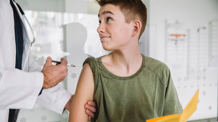 Symbolbild: Ein Teenager wird geimpft und hält seinen Impfausweis in der Hand. (Quelle: imago images/M. Fischinger)