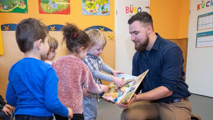 Symbolbild: Ein Erzieher im Kindergarten bespricht mit Kindern zur musikalischen Früherziehung ein Buch über Zootiere. (Quelle: dpa/B. Thissen)
