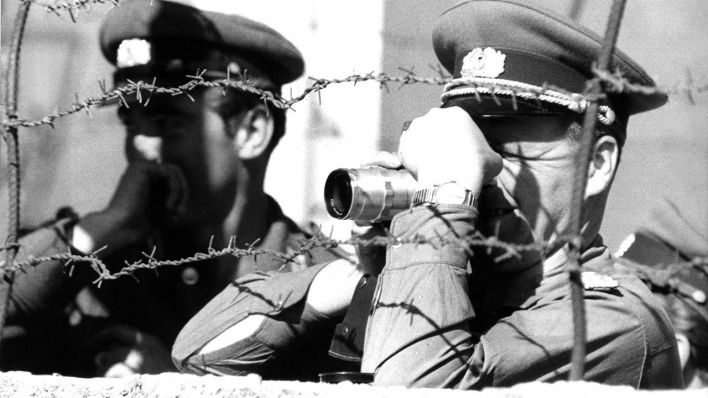 Ein Volkspolizist macht mit einer Kamera im Oktober 1961 in Berlin an der Sektorengrenze hinter einer Mauer mit Stacheldraht Erinnerungsfotos. (Quelle: dpa)