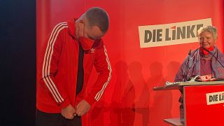 Klaus Lederer zieht sich am 18.08.2021 eine rote adidas-Jacke an. Katina Schubert schaut ihm dabei zu. (Quelle: rbb/Sebastian Schöbel)
