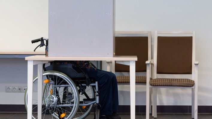 Eine Person im Rollstuhl gibt in der Wahlkabine eine Stimme ab (Bild: dpa/Robert Michael)