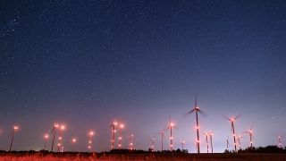 Unzählige Sterne leuchten am Nachthimmel einem hell beleuchteten Windenergiepark. (Quelle: dpa/Patrick Pleul)