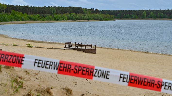 Mit einem Flatterband ist ein Zugang zum Strand des Helenesees abgesperrt. (Quelle: Patrick Pleul/dpa)