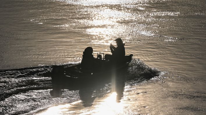 Zwei Angler fahren in einem Motorboot im Licht der Morgensonne auf dem deutsch-polnischen Grenzfluss Oder stromaufwärts. (Quelle: Patrick Pleul/dpa)