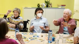 Eine Mitarbeiterin und Senioren in einem Pflegeheim sitzen um einen Tisch und spielen. (Quelle: dpa/Waltraud Grubitzsch)