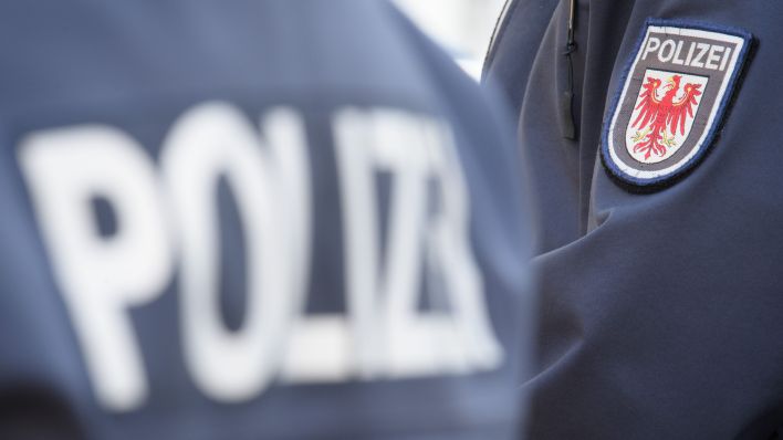 Das Logo der Brandenburger Polizei mit rotem Adler und Schriftzug auf dem Ärmel der Jacke einer Polizeibeamtin. (Quelle: Seren Stache/dpa)