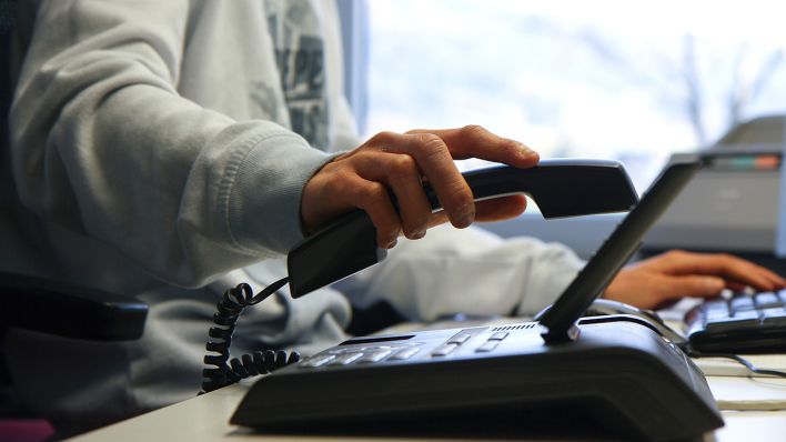 Symbolbild: Eine Person hält einen Telefonhörer einer Telefonanlage in der Hand (Bild: dpa/Eibner)
