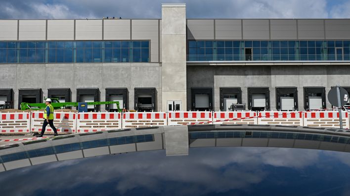 Eine Fabrikhalle der Tesla Gigafactory Berlin-Brandenburg spiegelt sich in einem Autodach wieder. (Quelle: dpa/Patrick Pleul)