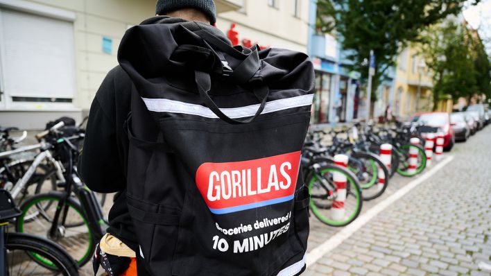 Symbolbild: Ein Beschäftigter des Lieferdienstes Gorillas trägt einen Rucksack und steht vor den Fahrrädern. (Quelle: dpa/A. Riedl)