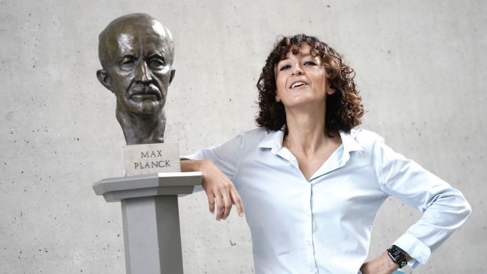 Die französische Genforscherin Emmanuelle Charpentier steht neben einer schrägen Büste von Max Planck.