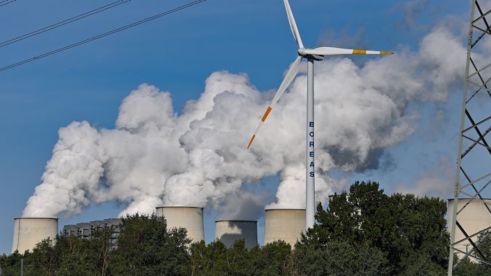 Wasserdampf steigt aus den Kühltürmen des Braunkohlekraftwerks Jänschwalde der Lausitz Energie Bergbau AG (LEAG). Davor steht eine einzelne Windenergieanlage und dreht sich im Wind. (Quelle: dpa/Patrick Pleul)