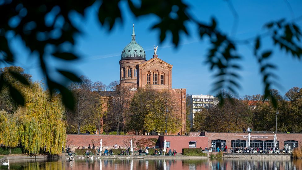 Die St. Michael Kirche und der Außenbereich des Café Engelbecken spiegeln sich bei sonnigem Wetter im Wasser. (Quelle: dpa/Monika Skolimowska)