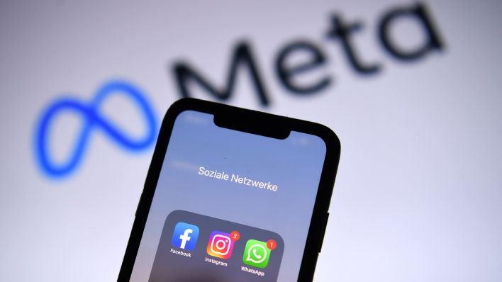 Ein Smartphone mit der Facebook-, Whatsapp- und Instagramm-App wird vor dem neuen Firmennamen "Meta" gehalten (Quelle: dpa/Revierfoto)