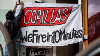 Ein Beschäftigter des Express-Lieferdiensts Gorillas klebt bei einer Demonstration vor der Firmenzentrale für bessere Arbeitsbedingungen ein Transparent mit der Aufschrift „Gorillas - We Fire in 10 Minutes“ an einer Wand fest. Quelle: dpa/Monika Skolimowska