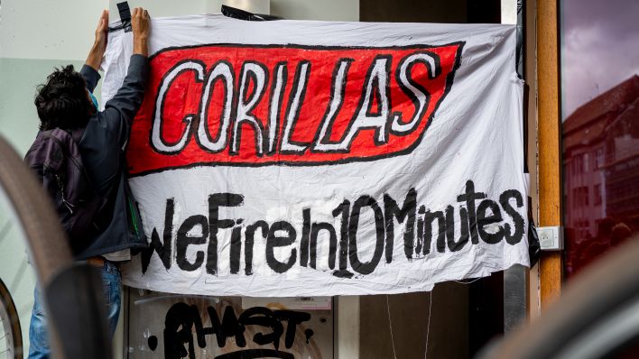 Ein Beschäftigter des Express-Lieferdiensts Gorillas klebt bei einer Demonstration vor der Firmenzentrale für bessere Arbeitsbedingungen ein Transparent mit der Aufschrift „Gorillas - We Fire in 10 Minutes“ an einer Wand fest. Quelle: dpa/Monika Skolimowska