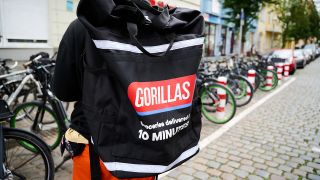 Ein Beschäftigter des Lieferdienstes Gorillas trägt einen Rucksack und steht vor den Fahrrädern. (Quelle: dpa/Annette Riedl)