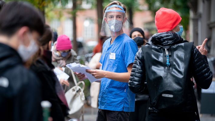 Arzthelfer Linus informiert Patienten in einer langen Schlange vor einer Arztpraxis im Berliner Bezirk Neukölln über den Corona-Test. (Quelle: dpa/Kay Nietfeld)