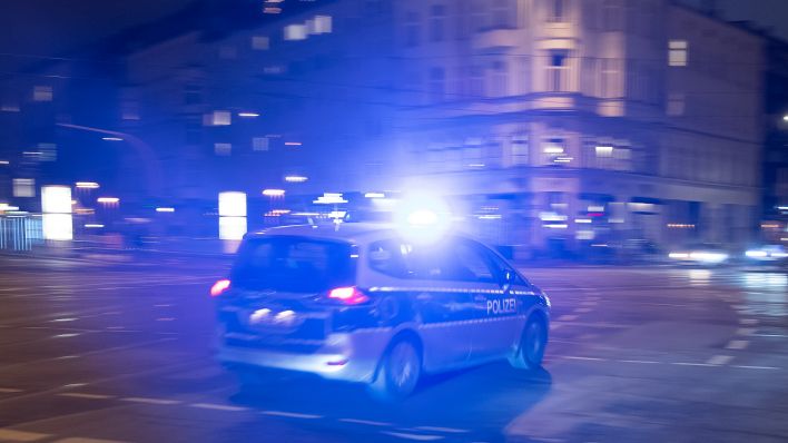 Ein Polizeifahrzeug fährt nachts in Berlin mit eingeschaltetem Blaulicht über eine Kreuzung. dpa/Paul Zinken
