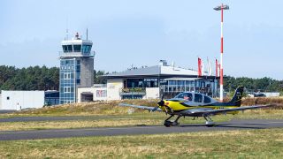 Archivbild: Ein Kleinflugzeug steht vor der Kulisse von Tower, Eingangsgebäude und Restaurant des Flugplatzes Schönhagen. (Quelle: dpa/S. Stache)