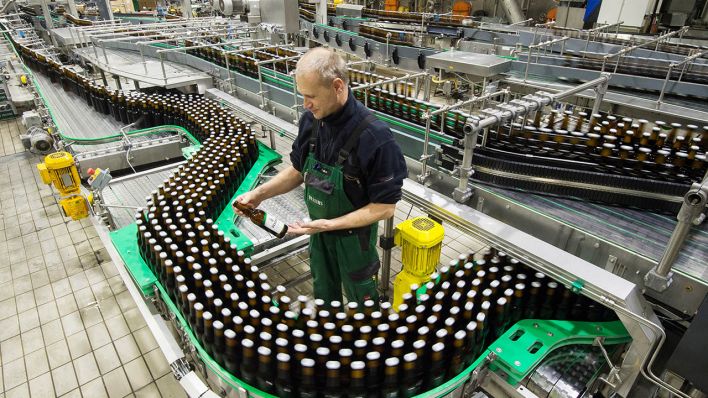 Archivbild: Ein Mitarbeiter kontrolliert in einer Befüllungsanlage der Veltins-Brauerei eine Bierflasche mit Kronkorken. (Quelle: dpa/R. Jensen)