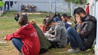 Migranten sitzen auf einer Wiese vor Containern in der Zentralen Erstaufnahmeeinrichtung für Asylbewerber in Eisenhüttenstadt. (Quelle: dpa/Patrick Pleul)