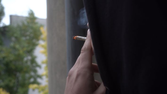 Anton steht auf einem Balkon und raucht einen Joint