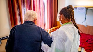 Ein Mann wird in einem Pflegeheim von einer Pflegekraft in Schutzkleidung mit Mundschutz und Shorts sowie Schutzbrille und Handschuhen betreut (Quelle: dpa/Robin Unrecht)